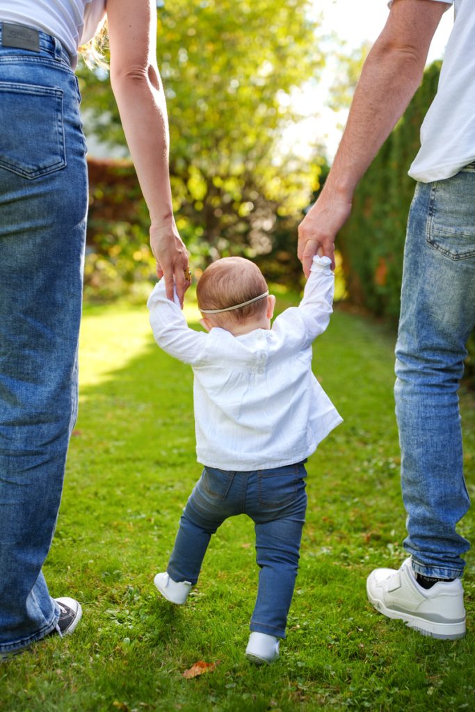 Un bébé qui marche de dos en tenant les mains de ses parents à Fonsorbes