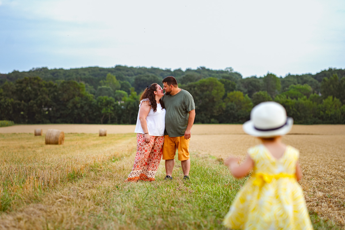 Une petite fille qui regarde ses parents s'embrasser lors d'une séance photo famille à Fontenilles