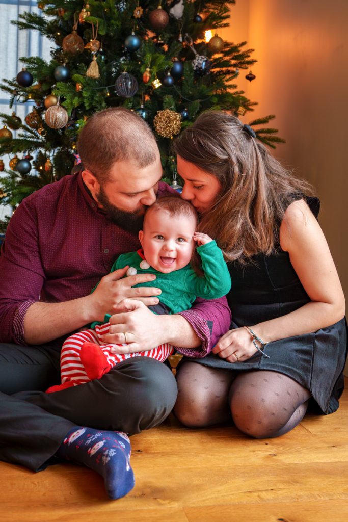 Des parents qui embrassent leur bébé à noël au pied du sapin à Colomiers