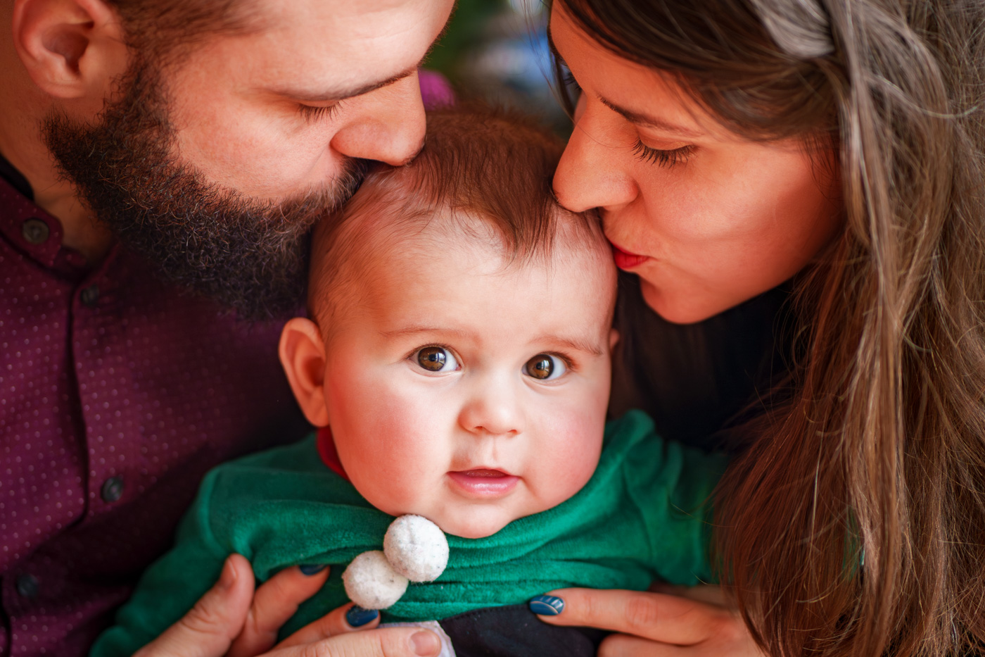 Deux parents qui embrassent la tête de leur bébé avec affection lors d'une séance famille à Plaisance du Touch