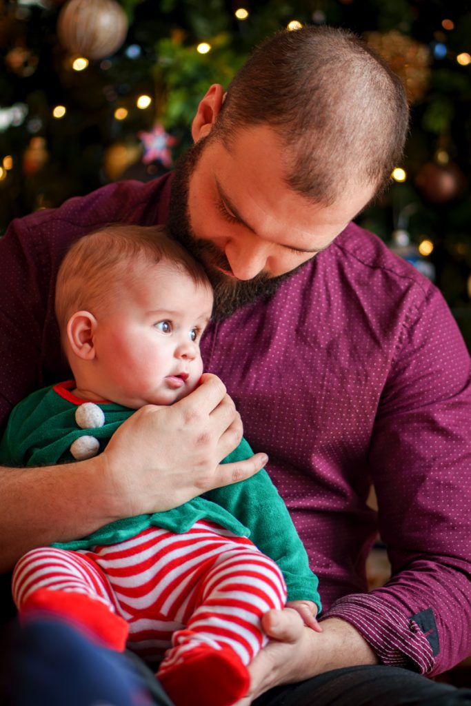 Un père qui tient son fils dans les bras devant le sapin de Nöel à Blagnac