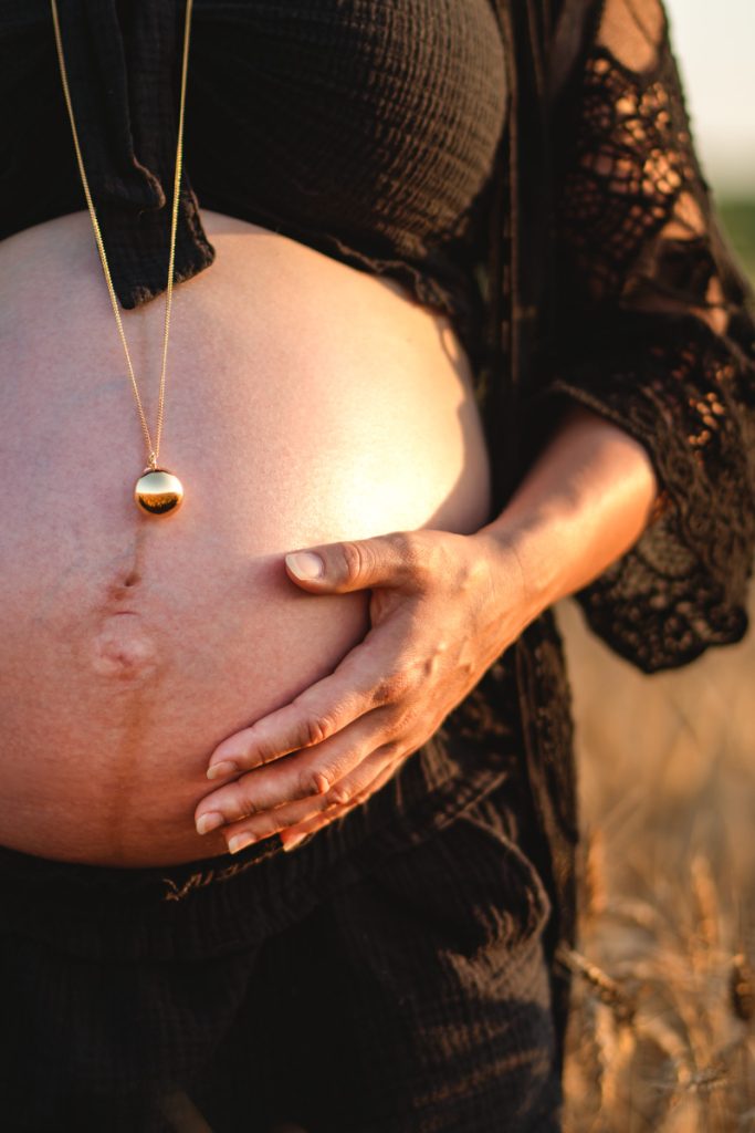 Séance photo grossesse : ventre rond d’une future maman au coucher du soleil dans les champs de blé, moment lumineux et naturel