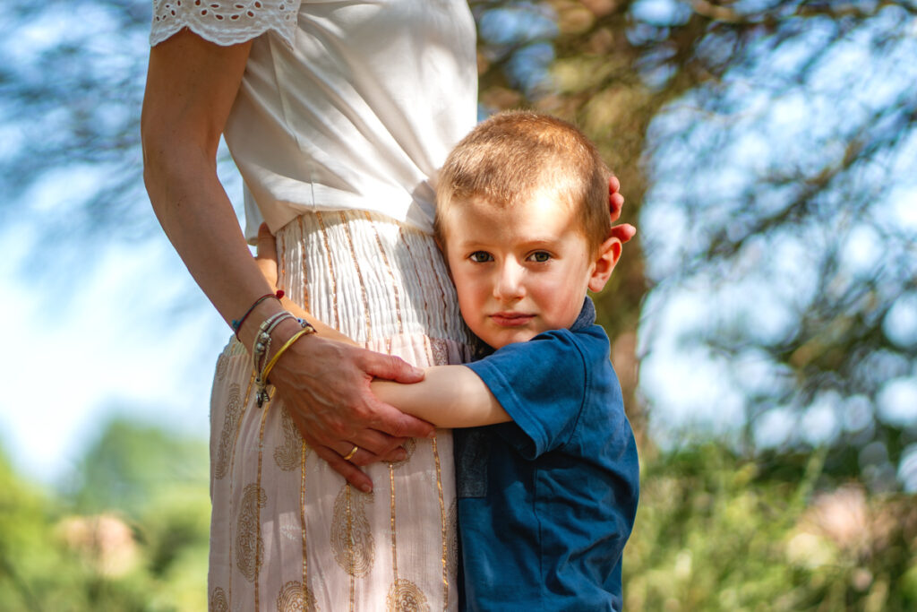 Un enfant qui serre la taille de sa mère dans ses bras et regarde l'appareil photo