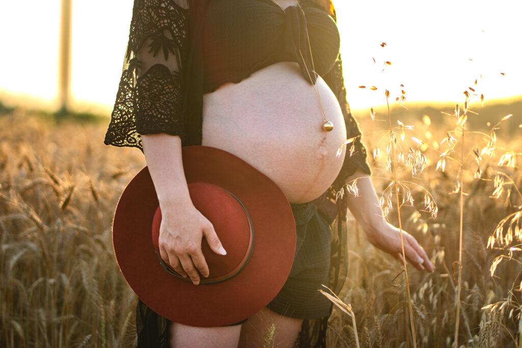ventre d'une femme enceinte qui tient un chapeau dans un champ de blé - séance photo grossesse à Plaisance du Touch