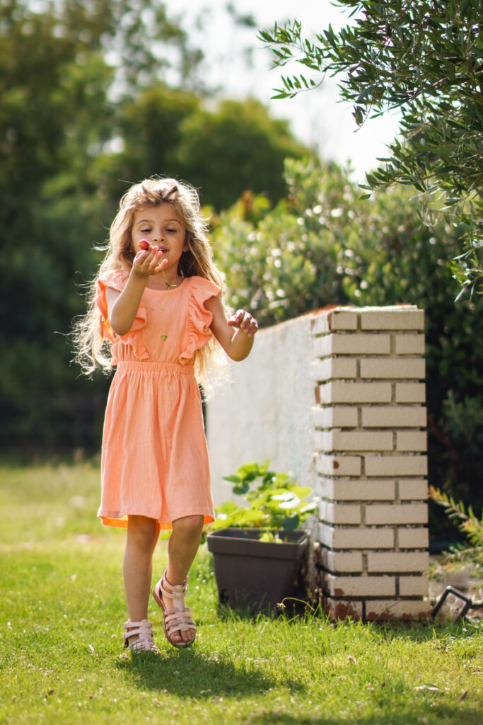 Une petite fille qui vient de cueillir une fraise - séance photo famille à Fontenilles