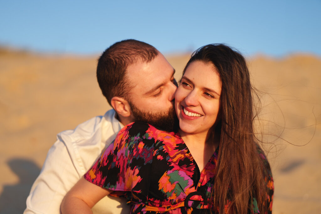 Un couple sur la plage où l'homme embrasse sa femme sur la joue lors d'une séance photo grossesse dans les landes
