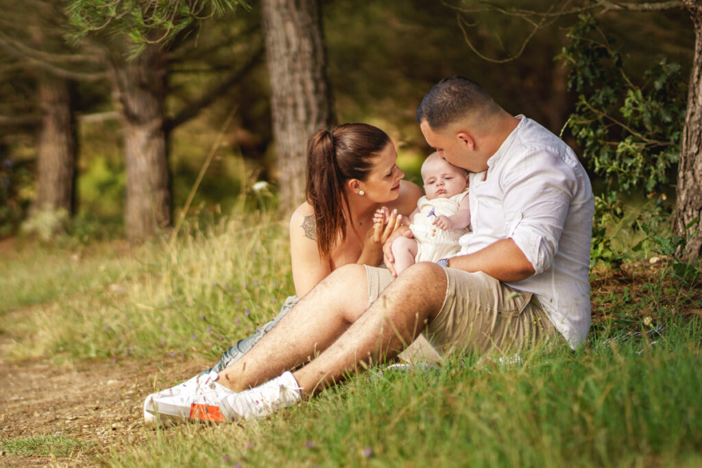 Un couple et leur bébé assis dans la nature lors d'une séance photo naissance à Toulouse